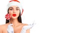 Christmas woman. Joyful model girl in Santa`s hat with lollipop candy pointing hand, proposing product. Surprised expression Royalty Free Stock Photo