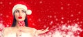 Christmas woman. Joyful model girl in Santa`s hat with lollipop candy pointing hand, proposing product. Surprised expression Royalty Free Stock Photo