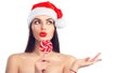 Christmas woman. Joyful model girl in Santa`s hat with lollipop candy pointing hand, proposing product. Surprised expression