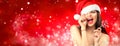 Christmas woman. Joyful model girl in Santa`s hat with red lips and lollipop candy in her hand