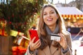 Christmas woman smiling at the camera holding smartphone and credit card in her hands with Christmas tree and markets on the Royalty Free Stock Photo