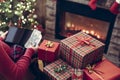 Christmas. Woman in sweater with tablet and american dollars searching gift sitting at table near fireplace and christmas tree. Royalty Free Stock Photo