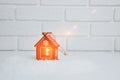 Christmas wooden toy in the form of a red house on artificial snow with a yellow light on a white background Royalty Free Stock Photo