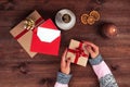 Christmas workplace top view. GirlÃ¢â¬â¢s hands on the wooden table holding Christmas preset. Christmas wreath, decorations