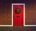 Christmas wreath on red front door with welcome mat.