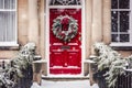 Christmas wreath and decoration on a classic red door on snowing winter holiday, Merry Christmas and Happy Holidays wishes, Royalty Free Stock Photo