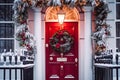 Christmas wreath and decoration on a classic red door on snowing winter holiday, Merry Christmas and Happy Holidays wishes, Royalty Free Stock Photo