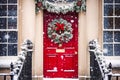 Christmas wreath and decoration on a classic red door on snowing winter holiday, Merry Christmas and Happy Holidays wishes, Royalty Free Stock Photo
