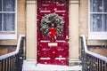 Christmas wreath and decoration on a classic red door on snowing winter holiday, Merry Christmas and Happy Holidays wishes, Royalty Free Stock Photo