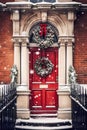 Christmas wreath and decoration on a classic red door on snowing winter holiday, Merry Christmas and Happy Holidays wishes, Royalty Free Stock Photo