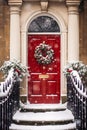 Christmas wreath and decoration on a classic red door on snowing winter holiday, Merry Christmas and Happy Holidays wishes, Royalty Free Stock Photo