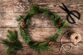 Christmas wreath of Fir branches, cones, scissors and skein of jute on dark wooden background.