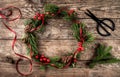 Christmas wreath of Fir branches, cones, scissors and skein of jute on dark wooden background.