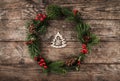 Christmas wreath of Fir branches, pine cones, berries and figurine of wood Christmas tree on rustic background.