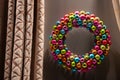 Christmas wreath made of colorful ornaments on gray wall with curtains