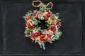 Christmas wreath made of fir branches, dried apples, cinnamon, red berries, bottle caps, red balls hanging on a black chalk board Royalty Free Stock Photo