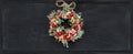 Christmas wreath made of fir branches, dried apples, cinnamon, red berries, bottle caps, red balls hanging on a black chalk board