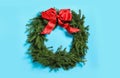 Christmas wreath made of fir branches with red bow on light blue background Royalty Free Stock Photo