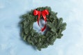 Christmas wreath made of fir tree branches with red ribbon on light blue textured background Royalty Free Stock Photo