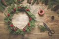 Christmas wreath made of spruce branches with holly berries on wooden board. Wreath workshop. Top view. Royalty Free Stock Photo