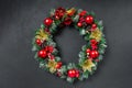 A Christmas wreath with a red bow and decorations of cones, holly, mistletoe, and winter greenery against a dark blue Royalty Free Stock Photo
