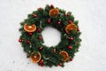Christmas wreath with red spruce balls and dry citrus slices on a background of white snow Royalty Free Stock Photo