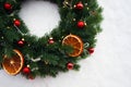 Christmas wreath with red spruce balls and dry citrus slices on a background of white snow Royalty Free Stock Photo