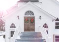 Christmas Wreaths Hang from Entrance Doors of Rustic Church In Winter Snow Scene