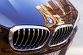 Chrome BMW logo sign close-up. Car grill and front hood of black blue BMW on an outdoor parking on a sunny day. City reflections Royalty Free Stock Photo