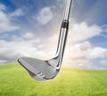 Chrome Golf Club Wedge Iron Against Grass and Blue Sky Background