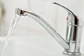 Chrome tap faucet with water flowing, blurred bathroom background Royalty Free Stock Photo