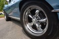 Chrome wheels gleam brightly on a blue sportscar under a sunny early summer day.