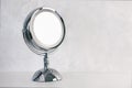 Chromed steel round magnifying mirror on handle set up on the table. Cold light background, the atmosphere of purity and cleanline