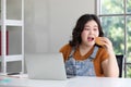 Chubby woman eating a hamburger while working from home Royalty Free Stock Photo