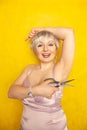 Chubby girl in dress with unshaven hairy armpits and scissors in hand on yellow background in Studio Royalty Free Stock Photo