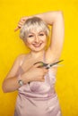 Chubby girl in dress with unshaven hairy armpits and scissors in hand on yellow background in Studio Royalty Free Stock Photo