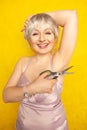 Chubby girl in dress with unshaven hairy armpits and scissors in hand on yellow background in Studio Royalty Free Stock Photo