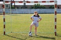 Chubby girl in sportswear stands in football gate and presses ball with her foot