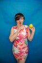 Chubby plus size woman holding green apple on blus studio solid background