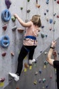 Chubby pretty Caucasian girl climbering artificial rock-climbing walls with trainer help and safety cable Royalty Free Stock Photo