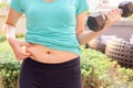 Chubby woman hand holding her own belly and dumbbell for exercising in public park. Royalty Free Stock Photo