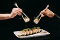 Chuka Roll in Chinese chopsticks in hands over the dish on a black background Royalty Free Stock Photo