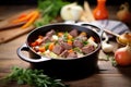 chunky beef stew in a cast iron pot, surrounded by raw ingredients