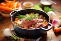 chunky beef stew in a cast iron pot, surrounded by raw ingredients Royalty Free Stock Photo