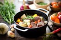 chunky beef stew in a cast iron pot, surrounded by raw ingredients Royalty Free Stock Photo