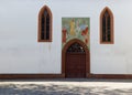 Church entrance with wooden door and religious mural, large historical stained glass windows, without people during the day