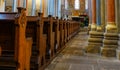 Church room of a medieval church with rows of wooden benches and coloured columns leading to the chancel with a magnificent