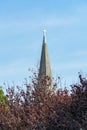 Church steeple with cross atop the pinnacle with blue and white lightly cloudy sky in late afternoon sun with gray roof