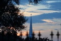 A church steeple silhouetted against a sunset sky with a wrought iron fence with crosses on top in the foreground