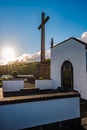 Churchyard with wall with iron door and large stone cross with mountains and sunbeams on the horizon, Vila Franca do Campo Azores